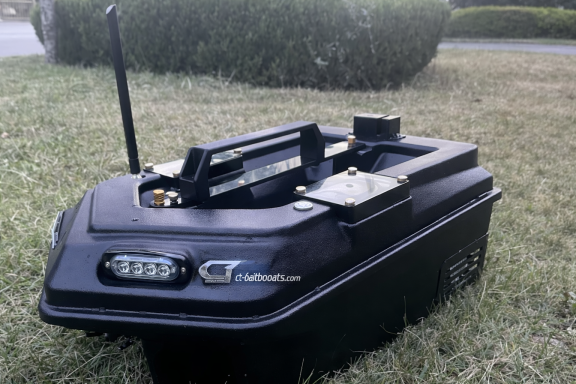 Schwarzes Modellboot mit Fernsteuerung auf grünem Gras.